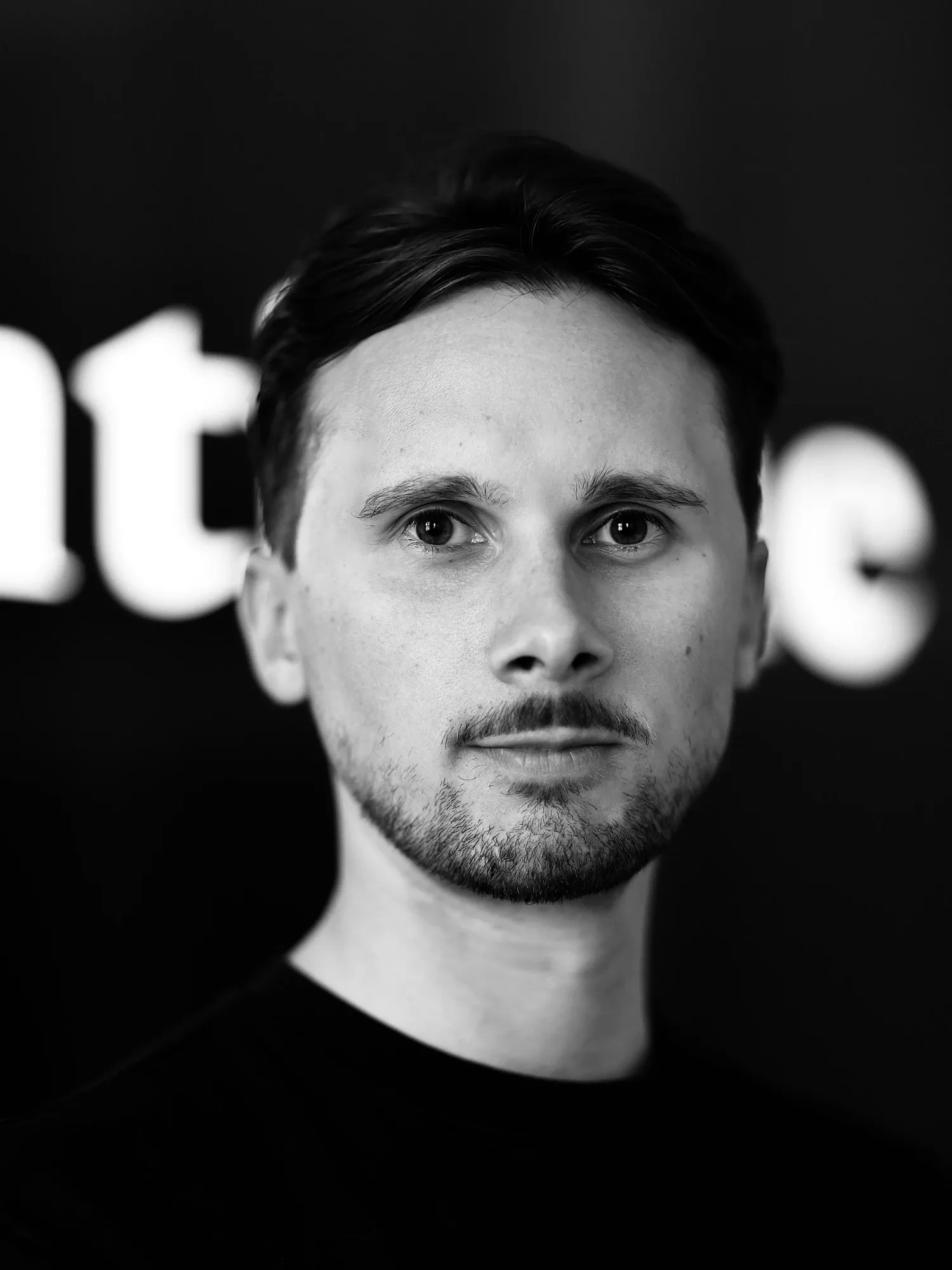 Justin Voigt, Gründer und Geschäftsführer von agentique. Schwarz-Weiß-Porträt vor einer dunklen Wand mit dem Schriftzug agentique.